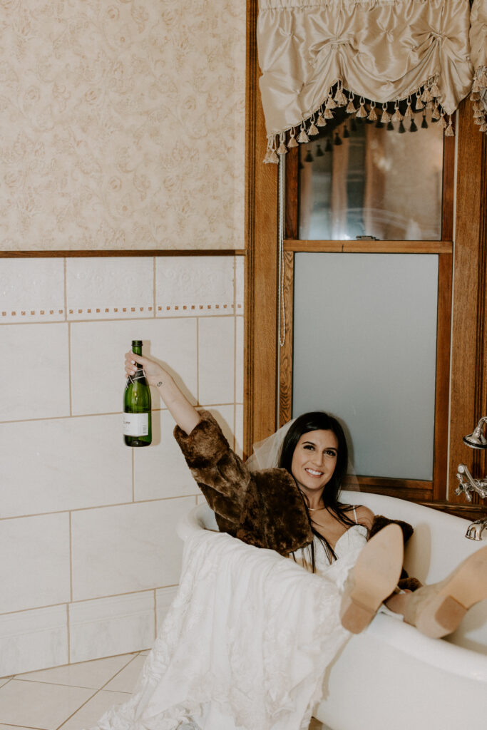 bride posing in bathtub with champagne in her wedding dress